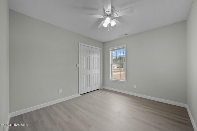 unfurnished bedroom with a textured ceiling, light wood-type flooring, a closet, and ceiling fan