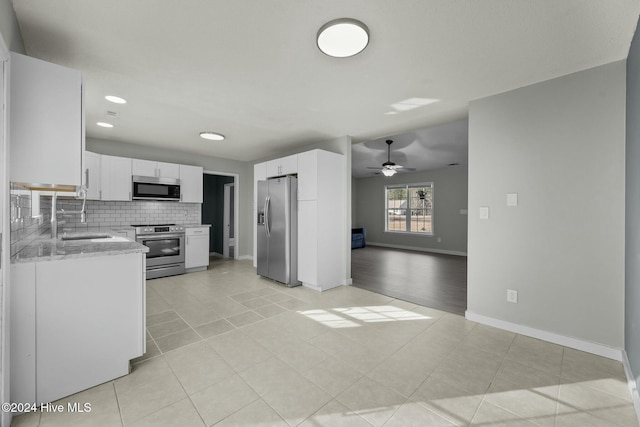 kitchen with sink, stainless steel appliances, light stone counters, backsplash, and white cabinets