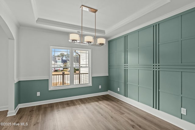 unfurnished dining area featuring ornamental molding, a tray ceiling, a chandelier, and light hardwood / wood-style floors