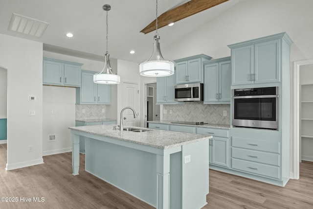 kitchen featuring sink, hanging light fixtures, an island with sink, stainless steel appliances, and light stone countertops