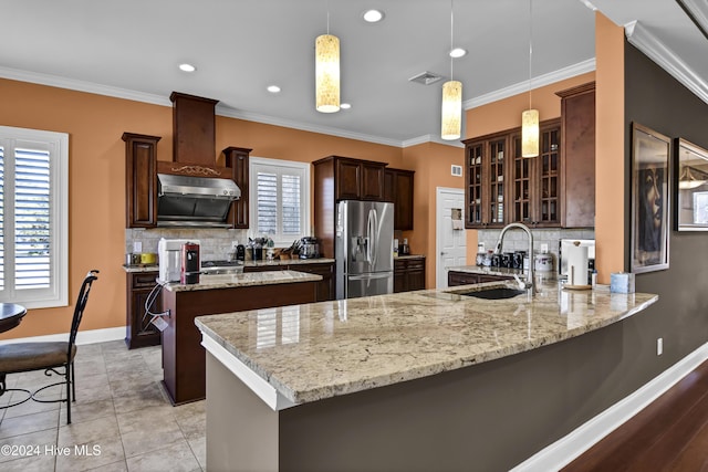 kitchen with kitchen peninsula, stainless steel refrigerator with ice dispenser, a healthy amount of sunlight, sink, and hanging light fixtures