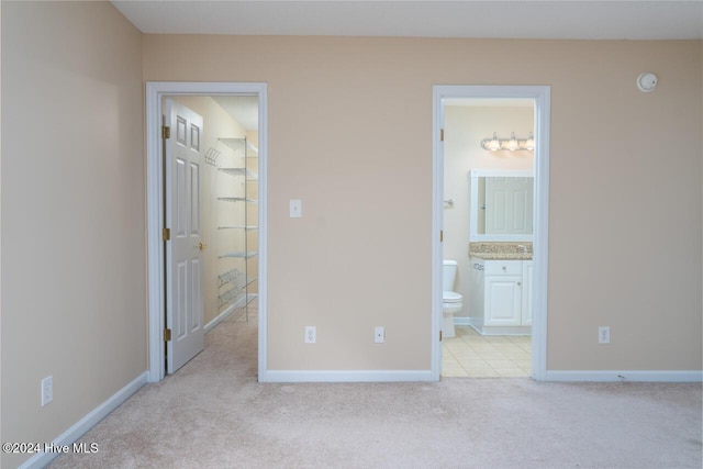 unfurnished bedroom with a spacious closet, light carpet, and connected bathroom