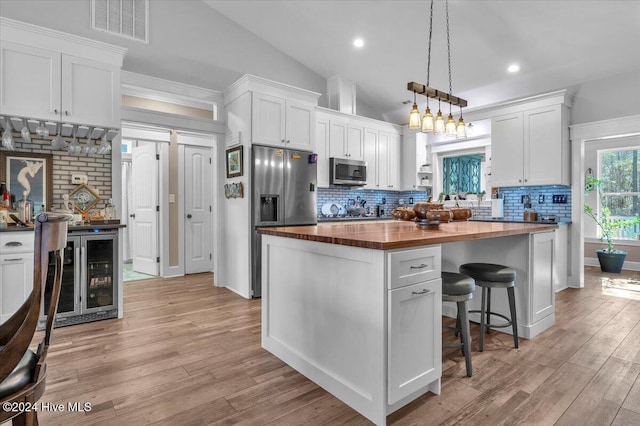 kitchen featuring beverage cooler, appliances with stainless steel finishes, a kitchen island, white cabinets, and butcher block counters