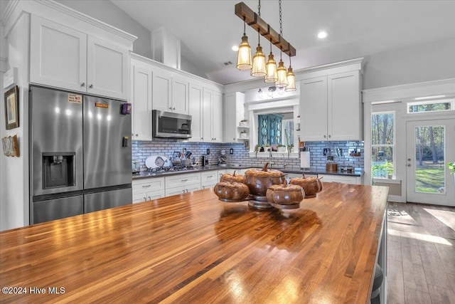 kitchen with hanging light fixtures, decorative backsplash, wood counters, white cabinets, and appliances with stainless steel finishes