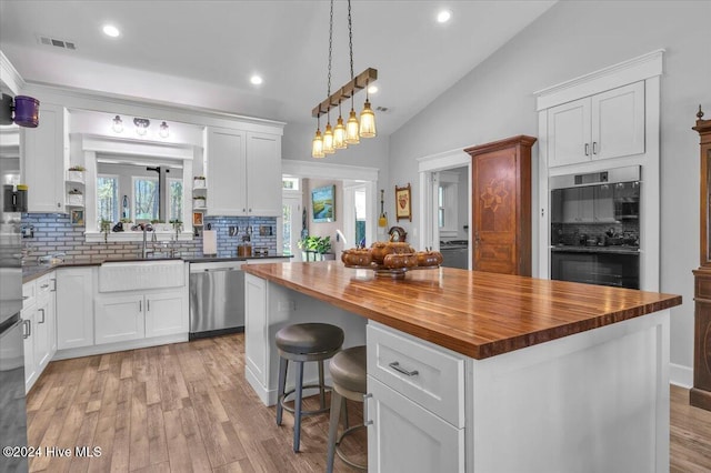 kitchen with butcher block counters, decorative backsplash, stainless steel dishwasher, and a center island