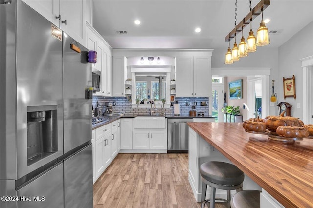 kitchen with decorative light fixtures, stainless steel appliances, butcher block countertops, and white cabinets