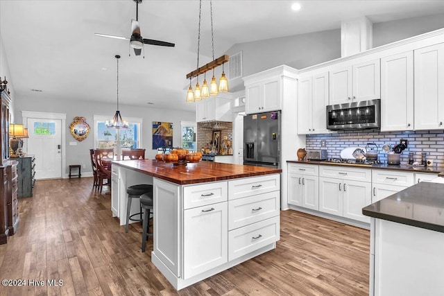 kitchen with appliances with stainless steel finishes, hanging light fixtures, a kitchen island, white cabinets, and tasteful backsplash