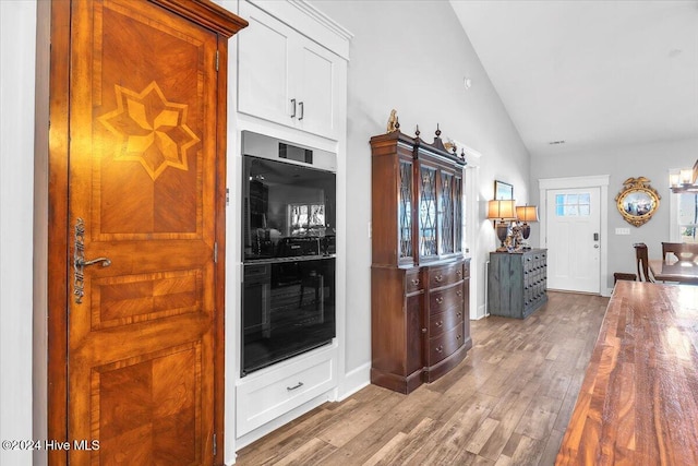 kitchen featuring vaulted ceiling, white cabinets, light wood-type flooring, and double oven