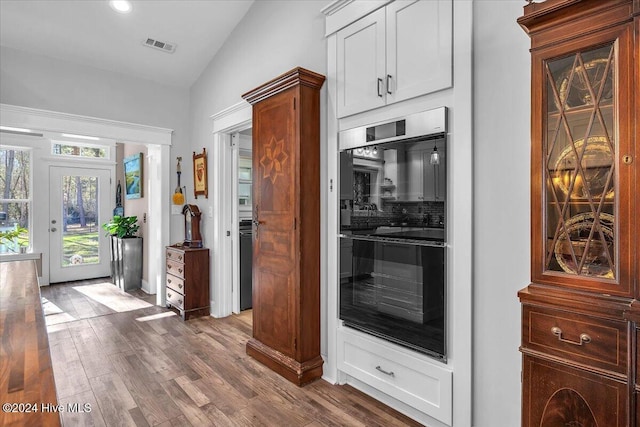 kitchen with white cabinetry, lofted ceiling, double wall oven, tasteful backsplash, and wood-type flooring