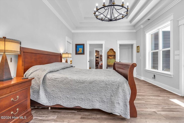 bedroom with a raised ceiling, a chandelier, light wood-type flooring, and ornamental molding