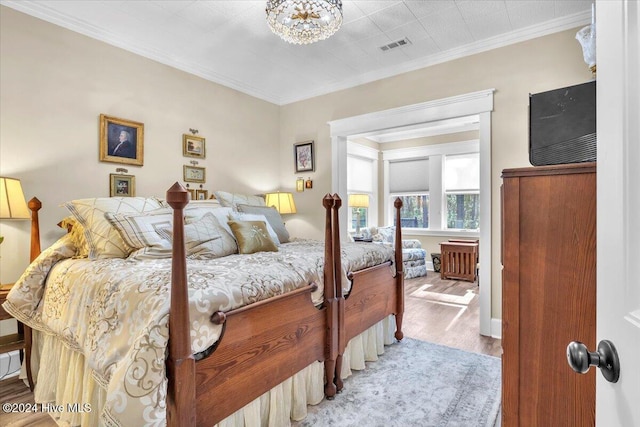 bedroom featuring a notable chandelier, light wood-type flooring, and crown molding