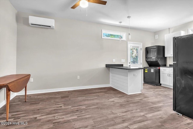 kitchen featuring white cabinets, black fridge, a wall mounted AC, and pendant lighting