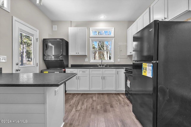 kitchen with black appliances, light hardwood / wood-style floors, sink, white cabinetry, and stacked washer and dryer