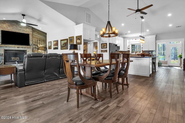 dining room featuring dark hardwood / wood-style floors, french doors, lofted ceiling, ceiling fan with notable chandelier, and a fireplace