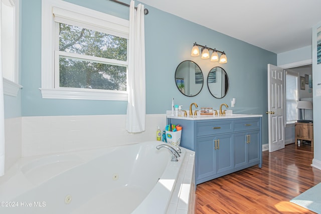 bathroom with hardwood / wood-style floors, vanity, and tiled bath