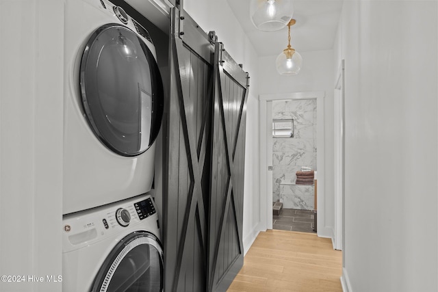 laundry room featuring a barn door, light wood-type flooring, and stacked washer / dryer