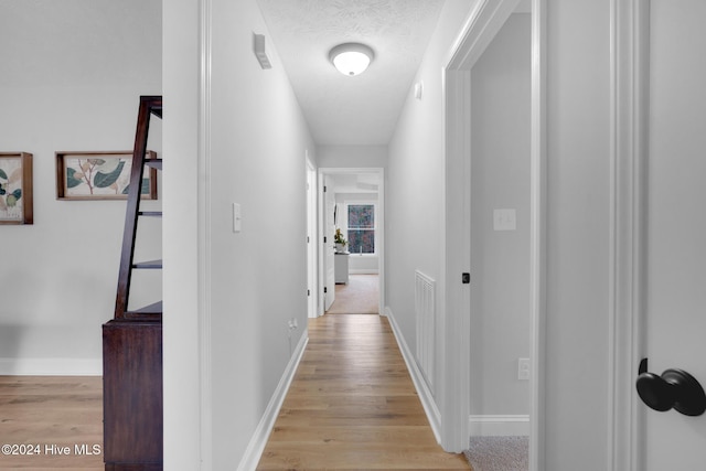 hall featuring light hardwood / wood-style flooring and a textured ceiling