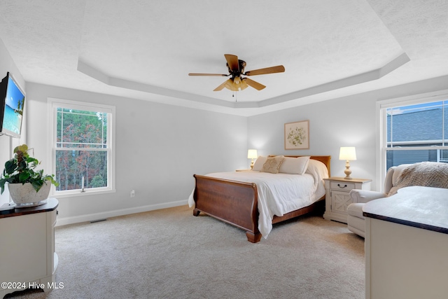 bedroom with a raised ceiling, ceiling fan, and light carpet