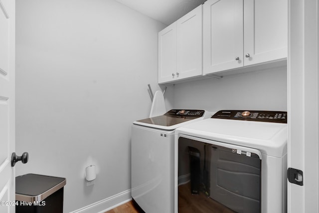 laundry room with washing machine and clothes dryer, cabinets, and wood-type flooring