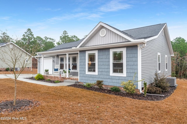 ranch-style home with central AC unit, a porch, a garage, and a front yard