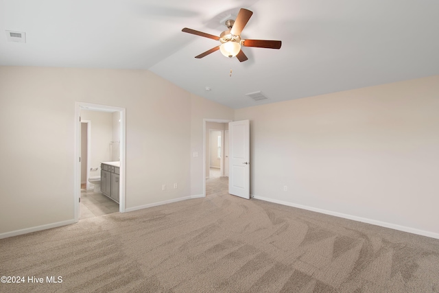 unfurnished bedroom featuring ceiling fan, light colored carpet, connected bathroom, and vaulted ceiling