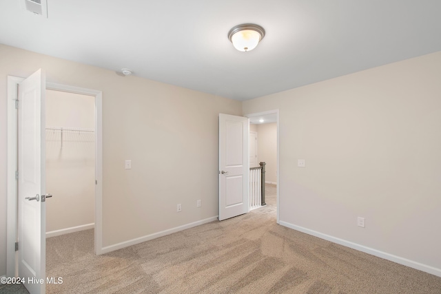 unfurnished bedroom featuring a spacious closet, light carpet, and a closet