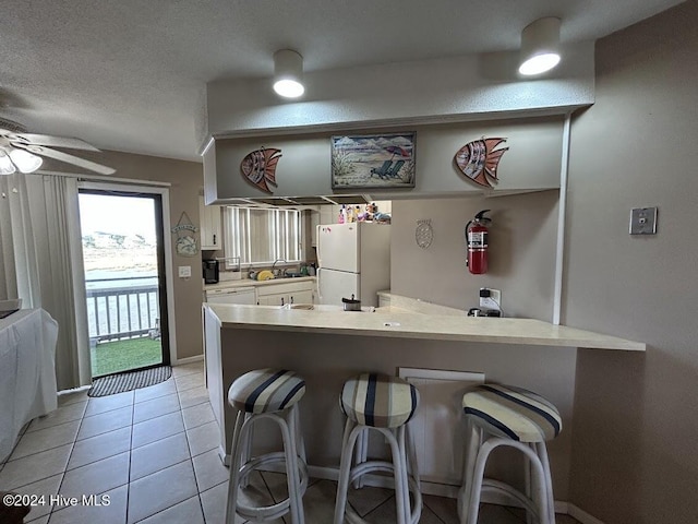 kitchen with kitchen peninsula, a kitchen breakfast bar, ceiling fan, white refrigerator, and light tile patterned flooring