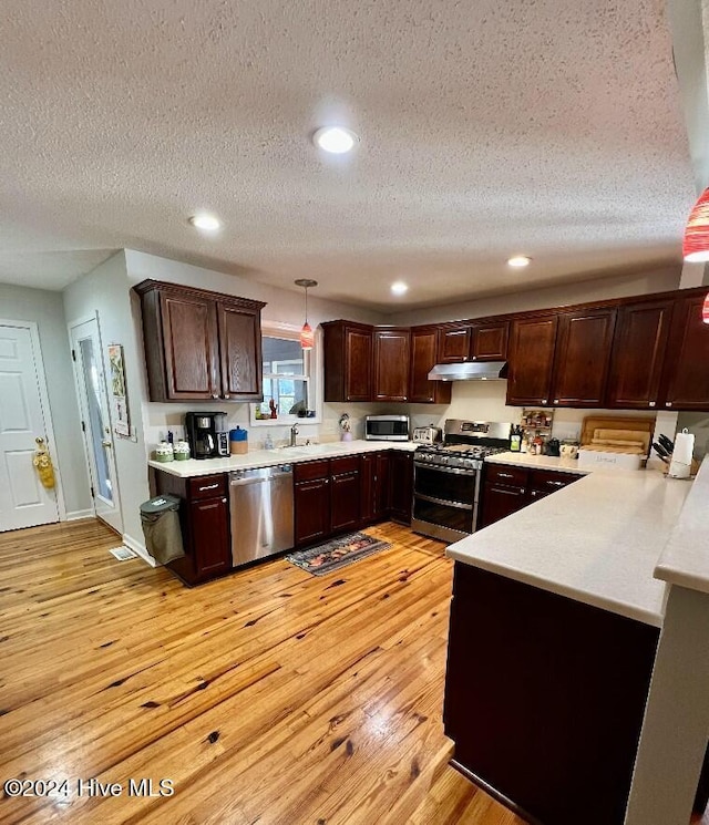 kitchen featuring appliances with stainless steel finishes, light wood-type flooring, decorative light fixtures, and a textured ceiling