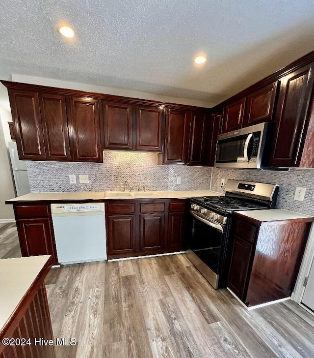 kitchen featuring appliances with stainless steel finishes, light wood-type flooring, backsplash, a textured ceiling, and sink