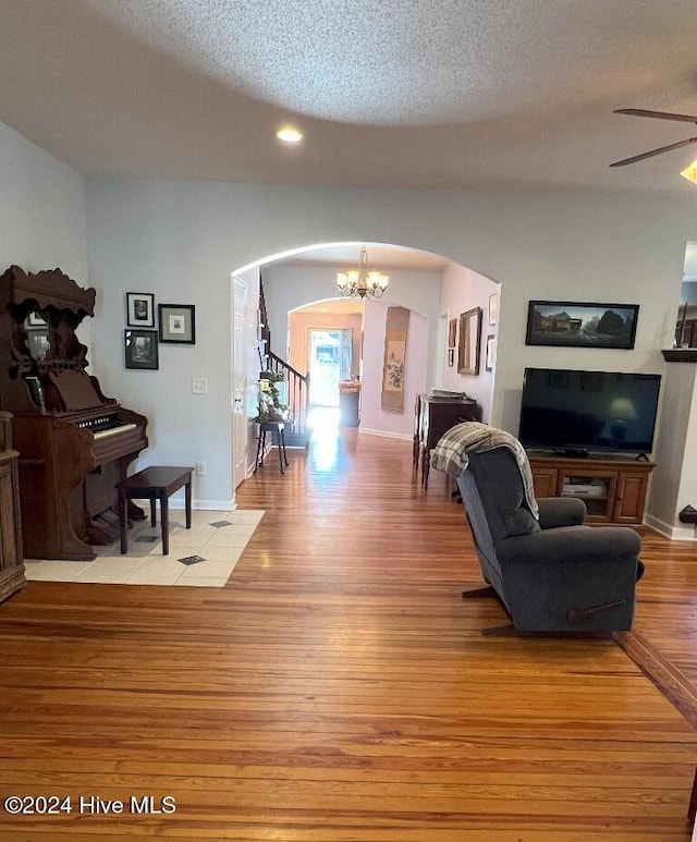 living room featuring ceiling fan with notable chandelier, a textured ceiling, and light wood-type flooring