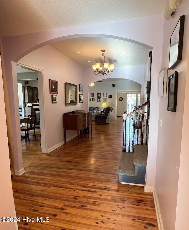 hall with wood-type flooring, a textured ceiling, and a chandelier