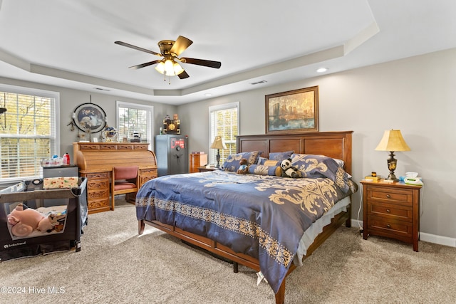 bedroom with a raised ceiling, ceiling fan, and light colored carpet