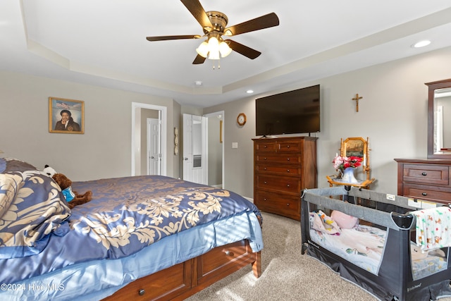 carpeted bedroom with ceiling fan and a tray ceiling