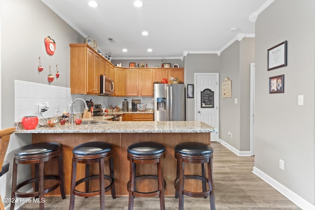 kitchen with light stone countertops, stainless steel appliances, light hardwood / wood-style flooring, backsplash, and crown molding