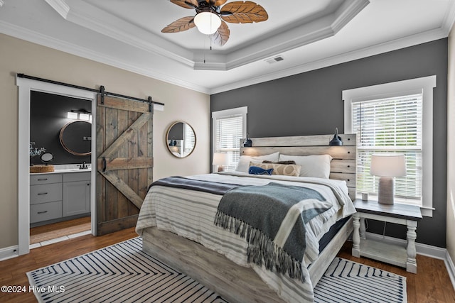 bedroom with connected bathroom, ceiling fan, dark wood-type flooring, a barn door, and ornamental molding