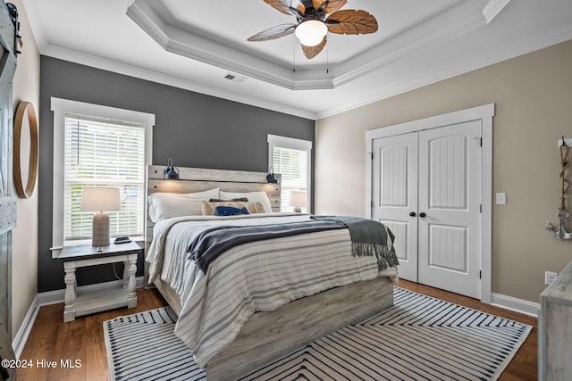 bedroom with a raised ceiling, ceiling fan, crown molding, dark hardwood / wood-style floors, and a closet