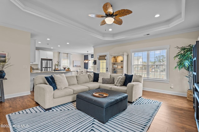 living room with light wood-type flooring, a raised ceiling, ceiling fan, and crown molding