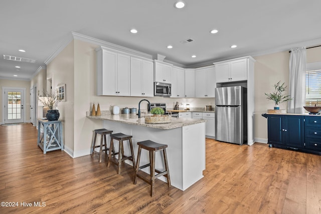 kitchen with appliances with stainless steel finishes, light hardwood / wood-style floors, white cabinetry, and a healthy amount of sunlight