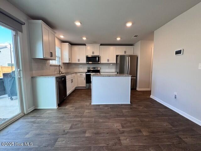 kitchen with a kitchen island, appliances with stainless steel finishes, white cabinets, decorative backsplash, and dark wood-type flooring