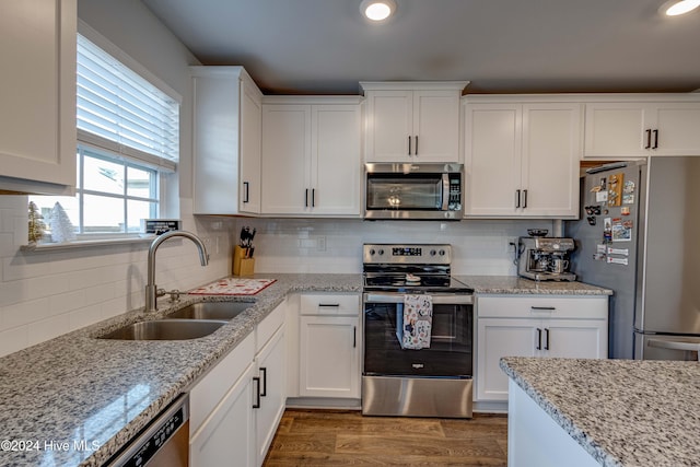 kitchen with sink, appliances with stainless steel finishes, white cabinetry, hardwood / wood-style floors, and light stone counters