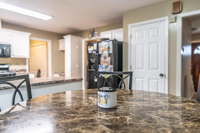 kitchen with dark stone counters, white cabinets, and black appliances