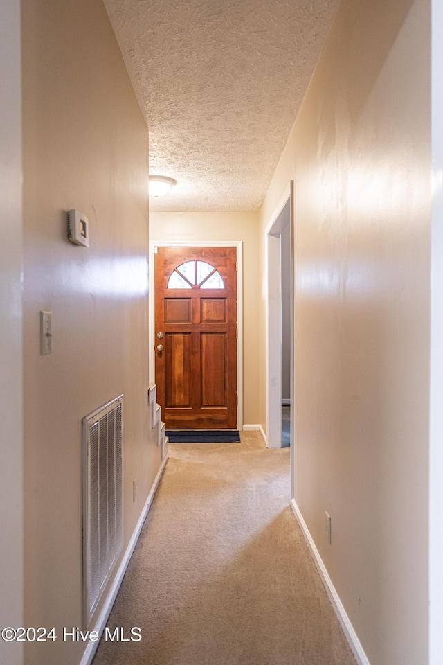 corridor with light colored carpet and a textured ceiling