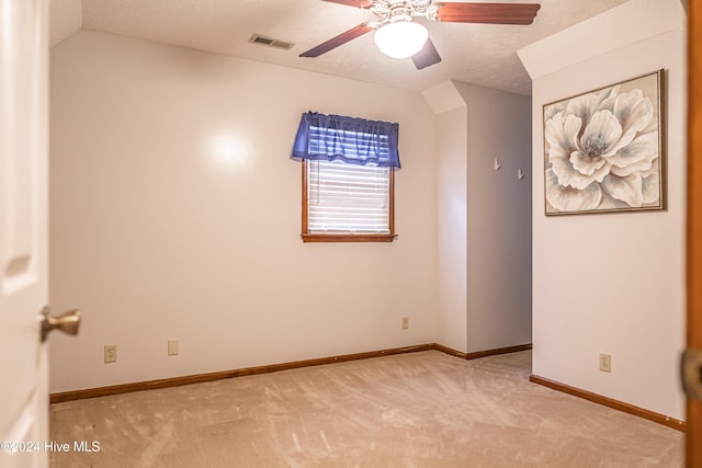 spare room with a textured ceiling, light colored carpet, and vaulted ceiling