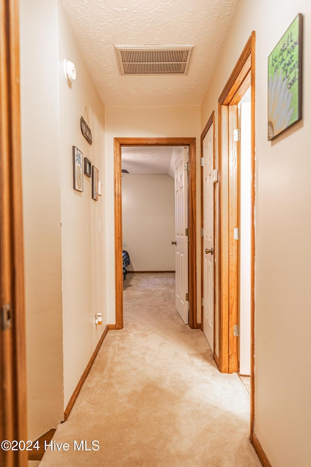 corridor with a textured ceiling and light colored carpet