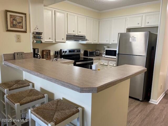 kitchen featuring kitchen peninsula, a breakfast bar, white appliances, crown molding, and white cabinetry