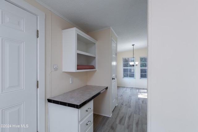 kitchen with pendant lighting, white cabinets, vaulted ceiling, light wood-type flooring, and a textured ceiling