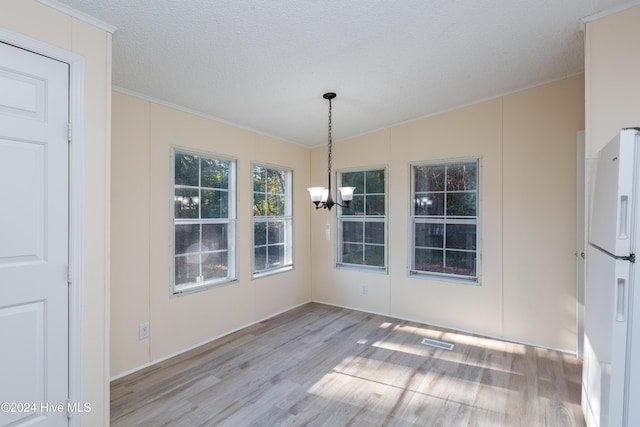 unfurnished dining area with a textured ceiling, light hardwood / wood-style floors, an inviting chandelier, and crown molding