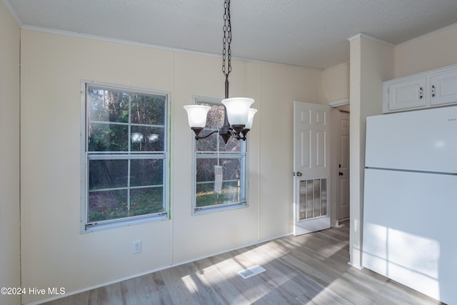 unfurnished dining area with crown molding, light hardwood / wood-style flooring, a textured ceiling, and a notable chandelier