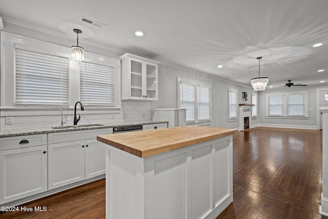 kitchen featuring butcher block countertops, decorative light fixtures, a center island, and white cabinetry