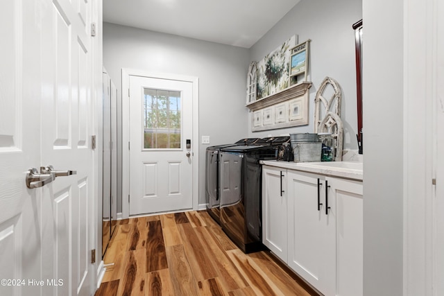 clothes washing area featuring cabinets, washing machine and clothes dryer, and light hardwood / wood-style floors